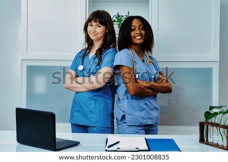 Portrait of two young women wearing medical scrubs with arms folded, looking at camera and smiling