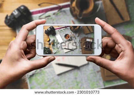 Hand taking photo with smart phone, travel concept flat lay. Map, coffee, passport, glasses, earphones, succulent, pencils, notebook, camera and film rolls on the table. 