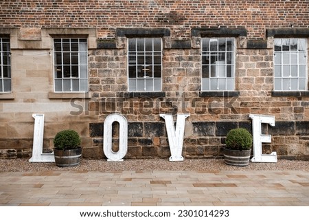 LOVE wooden letters outdoors in beautiful romantic courtyard with stone wall and widows for wedding ceremony.