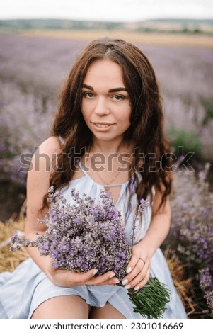 Beautiful girl hold bouquet purple lavender flowers in field. Female hold bouquet flowers collect lavender. Woman sits in lavender field. Enjoy floral glade, summer. Closeup. Natural cosmetics concept
