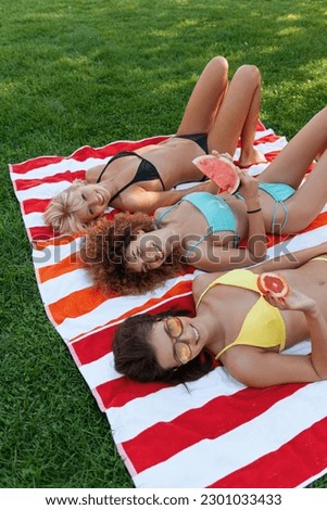 Three young women happy and smiling, eating fruit, enjoying on their towels. 