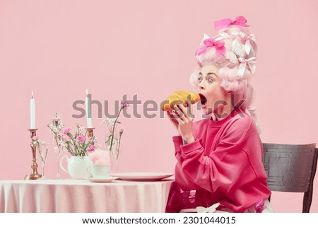 Portrait with surprised princess, queen wearing big wig and starting eat huge croissant on pink background with astonished face. Concept of food, diet, comparison of eras, modernity and renaissance