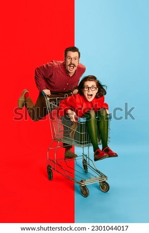 Crazy family. Portrait with funny couple, man and attractive woman sitting at shopping cart and racing on blue background. Concept of fun, human emotions, love, relationship, adventures, sales Royalty-Free Stock Photo #2301044017