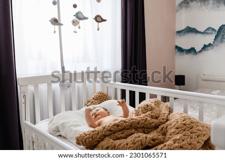 Cute newborn baby lying in the crib at home. Child looking at mobile for the cradle. Royalty-Free Stock Photo #2301065571