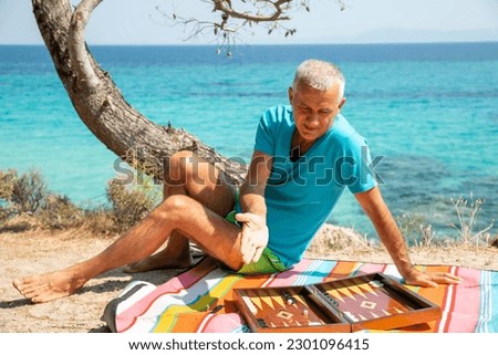 Middle-aged man rolling the dice on the beach, while playing backgammon board game
