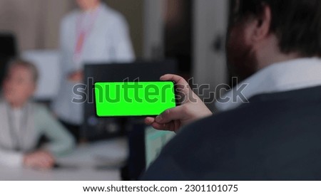 Back view of male manager looking at smartphone green screen sitting in office. Businessman have video conference on cellphone 
