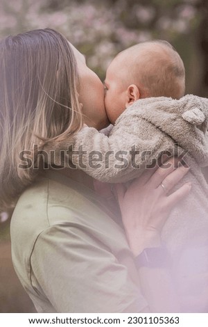 A charming boy in nature among flowering trees in his mother's arms. A child of 4 months plays with his mother and smiles. Family, pregnancy and childbirth.