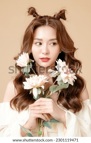 Young Asian beauty woman curly long hair with korean makeup style on cute face and perfect skin holding flowers on isolated beige background. Facial treatment, Cosmetology, plastic surgery.