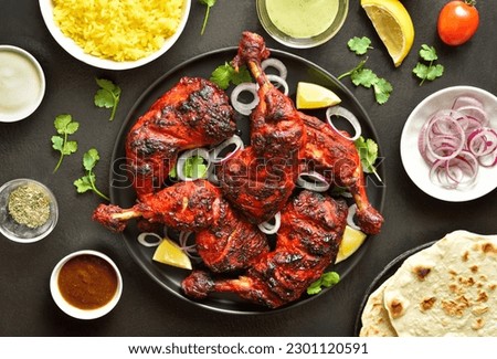 Indian style tandoori chicken on plate over dark stone background. Chicken legs marinated in yogurt and spices. Top view, flat lay Royalty-Free Stock Photo #2301120591