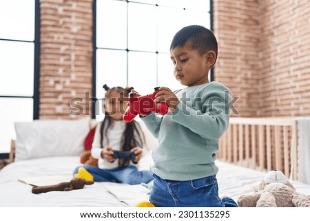 Adorable boy and girl playing video game sitting on bed at bedroom