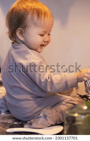 One-year-old baby sitting on her lap on the kitchen table and fiddling in flour