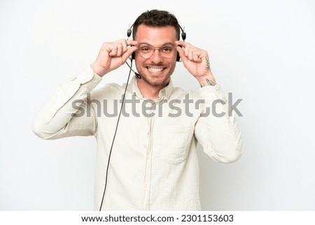 Telemarketer caucasian man working with a headset isolated on white background with glasses and surprised Royalty-Free Stock Photo #2301153603