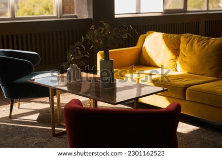Part of the interior with a yellow sofa and 2 armchairs, blue and red, magazine table and carpet. Window on the background, decor on the table, vases and copy space. High quality photo Royalty-Free Stock Photo #2301162523