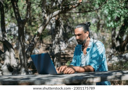 Male tourist working on a laptop outdoors in a camping. Young guy, freelancer working online at a laptop computer on a hike in the mountains outdoors. The ability to work from anywhere in the world. Royalty-Free Stock Photo #2301175789
