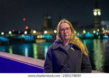 Blonde woman posing in front of illuminated Houses of Parliament at night.