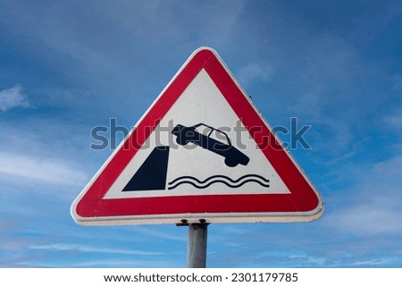 Car falling into the water danger sign against a blue sky