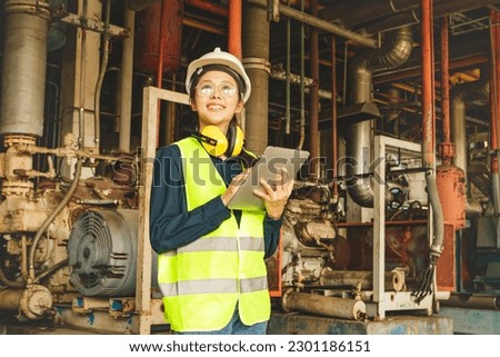 Asian female technician worker in engineering department wearing hard hat supervising machinery refrigeration system factory holding tablet checking control system standing and looking at work place. Royalty-Free Stock Photo #2301186151
