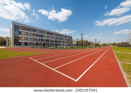 In the school yard: an red artificial turf running track and a soccer field with football goals Royalty-Free Stock Photo #2301197541