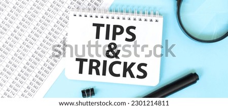 White notepad and magnifier on the financial documentation. Text TIPS AND TRICKS. Business concept