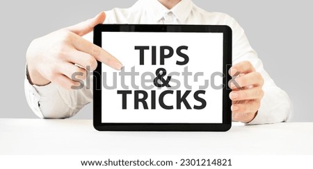 Text TIPS AND TRICKS on tablet display in businessman hands on the white background. Business concept