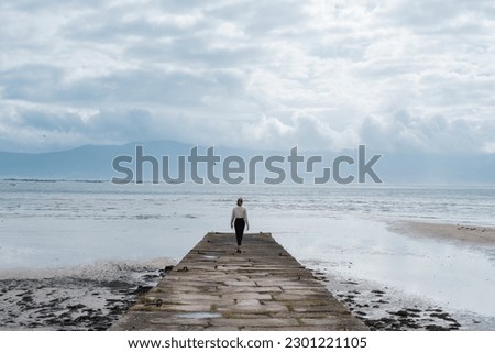 Unrecognizable woman walking on a dike near the calm sea. Concept. Relaxation, disconnection, happiness Royalty-Free Stock Photo #2301221105