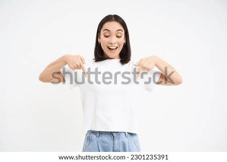 Portrait of beautiful smiling korean girl, points fingers down, shows advertisement, demonstrates banner below, isolated on white background.