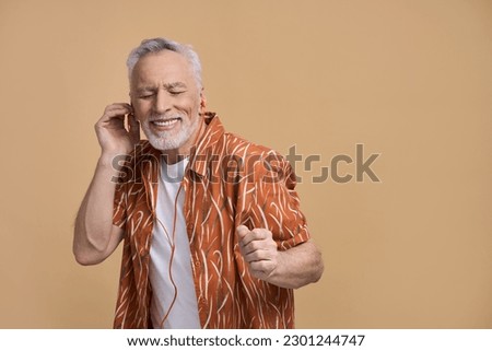 Stylish modern Caucasian happy retired senior man, gray haired active male tourist traveller, a joyful holiday maker smiling, enjoying summer vacation, listening to music on isolated beige background Royalty-Free Stock Photo #2301244747