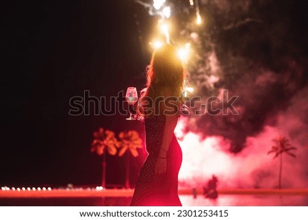A silhouette of a woman with a glass in front of fireworks