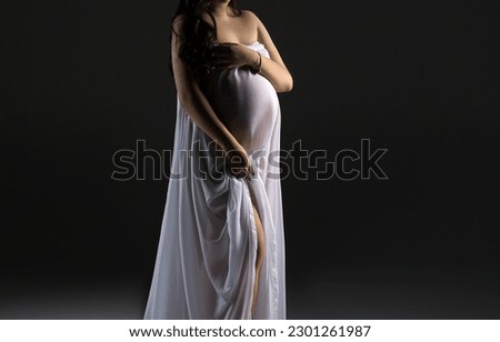 A pregnant woman in a white dress on a black background with a place for text. Studio pregnancy photo shoot. Stylish pregnancy.