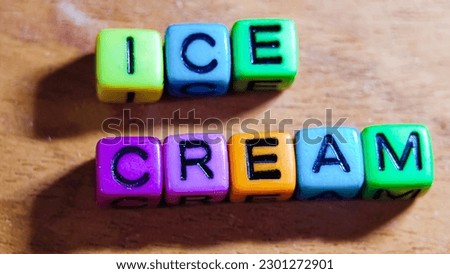 The word ICE CREAM is written in colorful plastic cuboid letters on a wooden background.