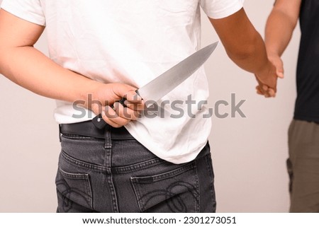 Two male shaking hand with one hand holding a knife on white background.Weak trust. Backstabbing friends.Man hold and hide knife at the back ready to kill.Blackmail and unreliable partnership concept.