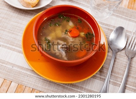 Hearty homemade soup with pork meat on bone and vegetables served with greens.