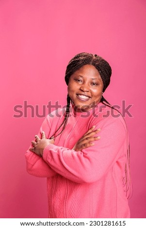 Portrait of friendly young adult standing in arm crossed while posing in studio over pink background, laughing at camera during shoot. Cheerful woman with joyful expression having fun, enjoying free
