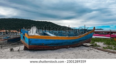 A small old boat anchored in the sand of a beach with a small hill in the background and some summer houses.