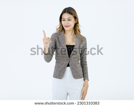 Isolated cutout studio shot of Millennial Asian successful professional female businesswoman in formal suit standing smiling holding hand pointing finger on blank empty space on white background.