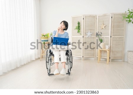 Asian woman in a wheelchair using a laptop in the living room
