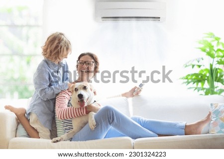 Mother and child with air conditioner remote control. Comfortable temperature at family home. Cooling and heating device. Mom and kid on couch under cold breeze. Air conditioning on hot summer day.  Royalty-Free Stock Photo #2301324223