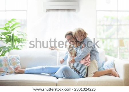 Mother and child with air conditioner remote control. Comfortable temperature at family home. Cooling and heating device. Mom and kid on couch under cold breeze. Air conditioning on hot summer day.  Royalty-Free Stock Photo #2301324225