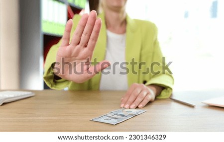 Portrait of female sitting in office and showing stop sign or protesting gesture. Woman denying proposal or bribe, making stop gesture with hand