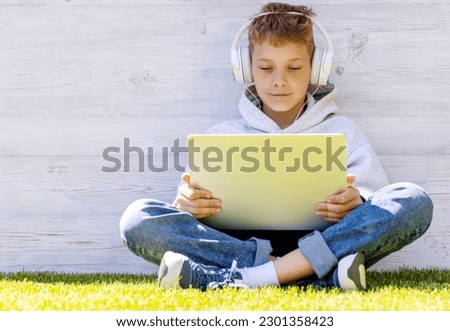 A boy using a laptop and headphones outdoors. Education or entertainment concept