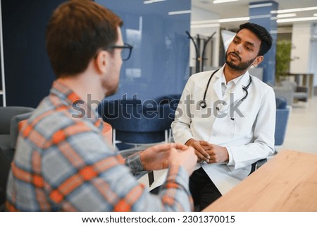 Indian doctor in white gown seeing patients in office Royalty-Free Stock Photo #2301370015