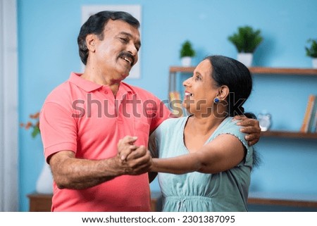 Happy senior couple dancing and singing by holding hands at home - concept of romantic, harmonious and active retirement lifestyle