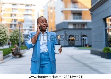 A young businesswoman walks to the office after a break with a coffee in her hand and talks on the phone Royalty-Free Stock Photo #2301394471