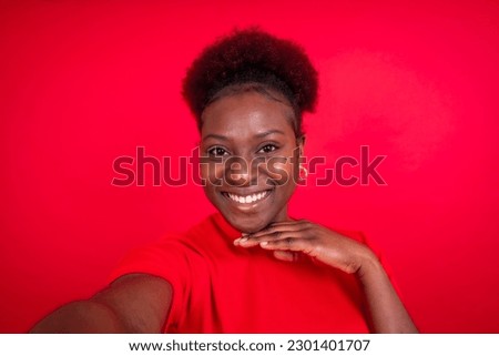 Young african american woman isolated on a red background smiling and making a selfie, studio shoot