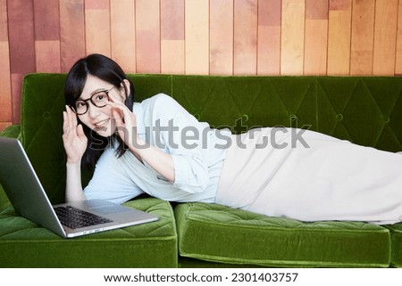 Asian woman relaxing on green sofa. Using a computer to look at something