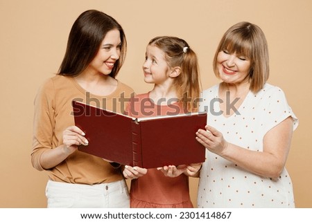 Happy smiling adorable fun women wear casual clothes with child kid girl 6-7 years old. Granny mother daughter read look at photo album isolated on plain beige background. Family parent day concept