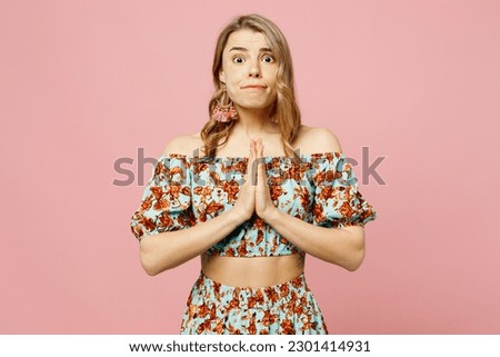 Young blonde caucasian woman wear summer casual clothes hold hands folded in prayer gesture, begging about something isolated on plain pastel light pink background studio portrait. Lifestyle concept