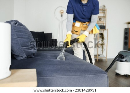Cleaning service worker vacuuming sofa from dust with vacuum cleaner during housework Royalty-Free Stock Photo #2301428931