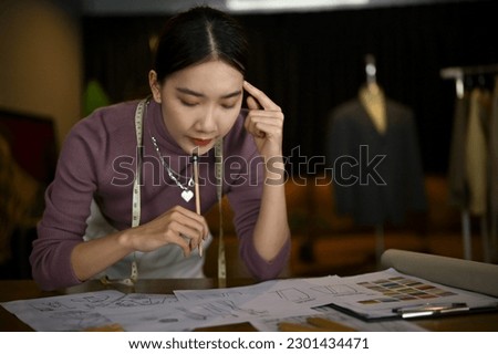 Professional Asian female fashion designer or tailor focuses on designing her new costume models and working on her new collection in a studio.