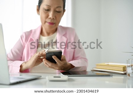 Close-up image of a senior Asian businesswoman using her smartphone at her office desk. chat, message, sms, email, social media